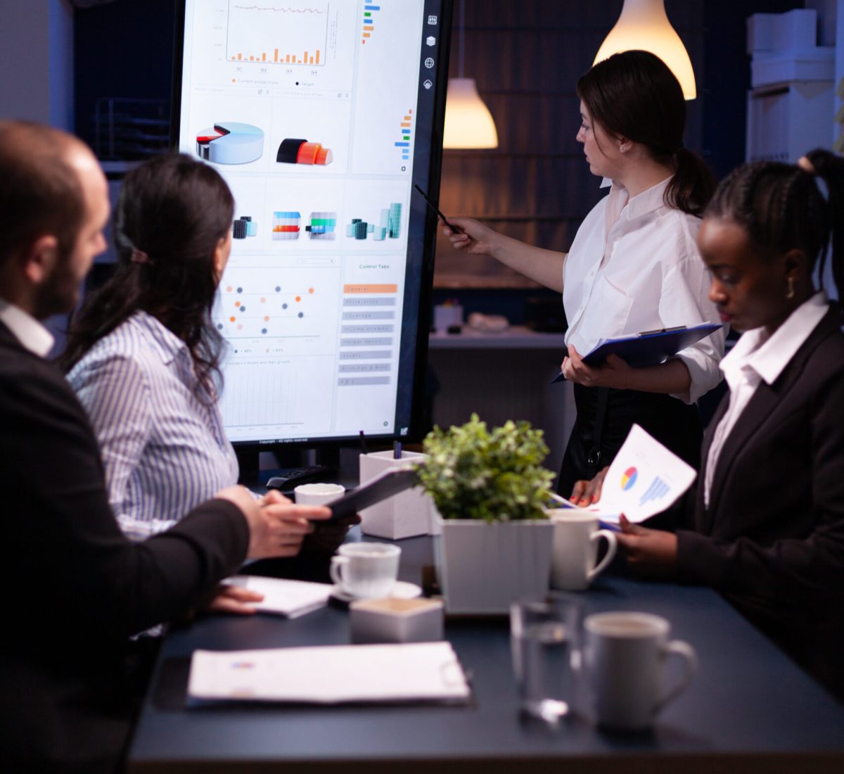 Diverse multiethnic business teamwork overworking in office meeting room analyzing financial graphs late at night. Coworkers brainstorming project ideas solving company problem.